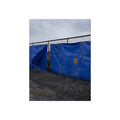 Blue tarps lashed to a chain link fence above gravel under grey sky. Drapery on the Fence by Garabaggio, fine art print, 12″ x 16″.
