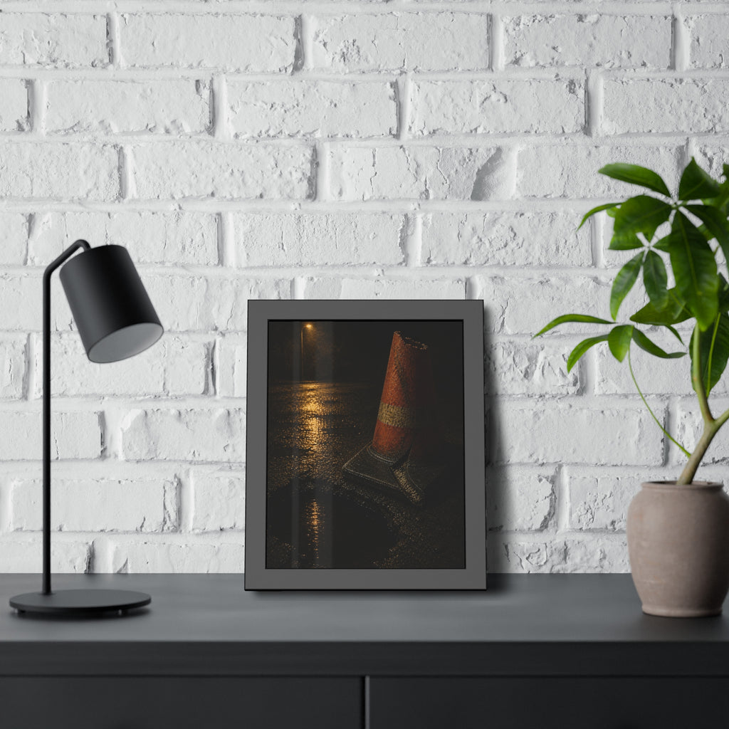 A traffic cone beside a water filled pothole reflecting a street lamp. The Sentinel of the Pothole by Garabaggio, framed fine art print hanging in a room.