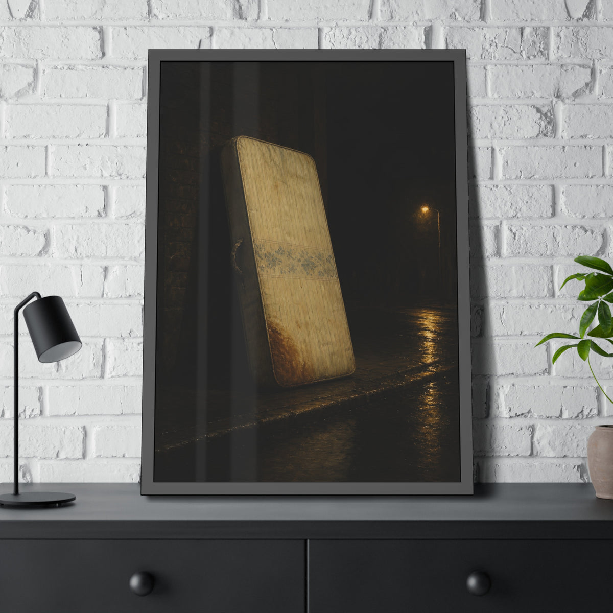A stained mattress propped on a brick wall along a wet night street. The Presentation Against the Brick by Garabaggio, framed fine art print hanging in a room.