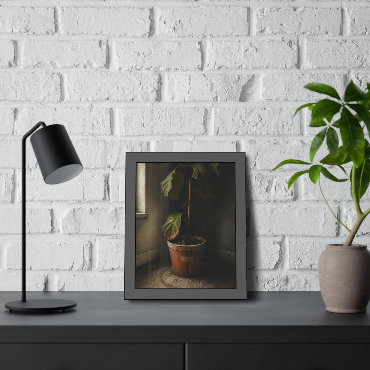 A leafy potted fig staked to a cane in a taped clay pot beside a window. The Corner by the Window by Garabaggio, framed fine art print hanging in a room.