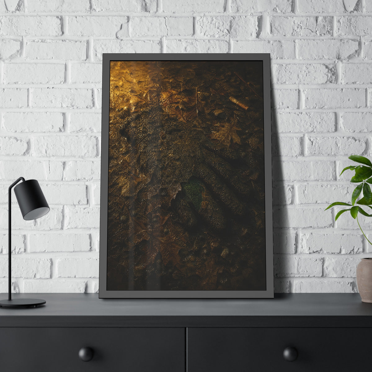 Wet mud and pressed oak leaves with a green scrap barely showing. The Reliquary of Mud and Leaf by Garabaggio, framed fine art print hanging in a room.