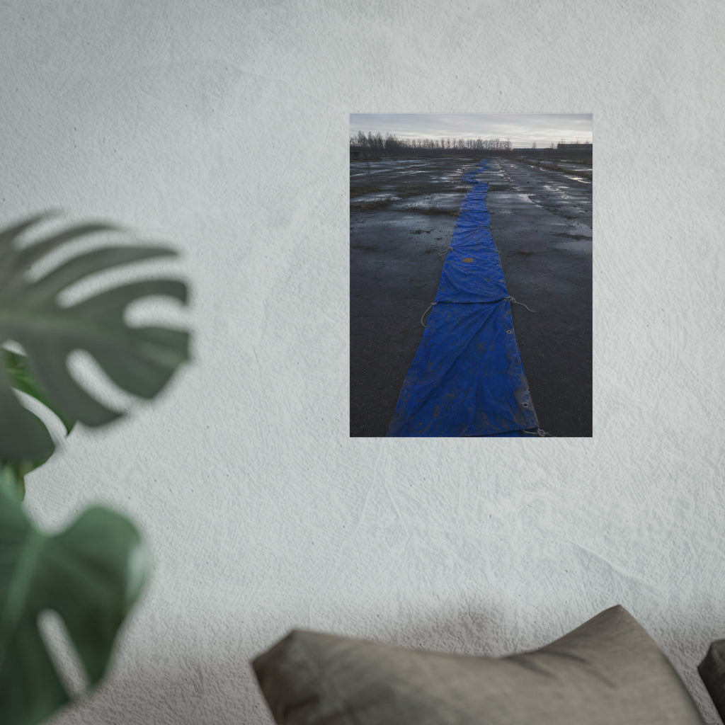 A blue tarp laid in a long strip down a wet cracked lot under grey sky. The Long Ground Procession by Garabaggio, fine art print hanging in a room.
