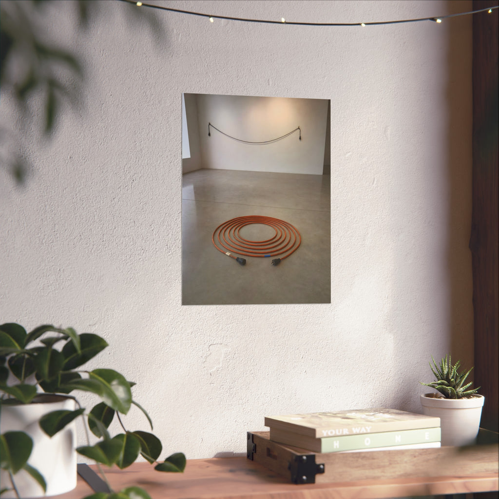 An orange extension cord coiled in a spiral on a bare gallery floor. The Floor Coil by Garabaggio, fine art print hanging in a room.
