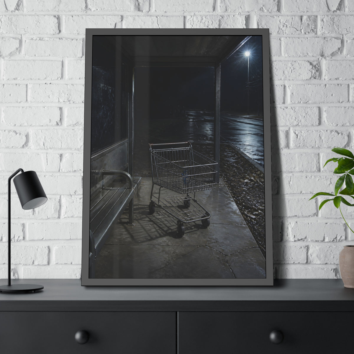 A shopping cart parked inside a bus shelter under a street lamp at night. The Rest at the Bus Shelter by Garabaggio, framed fine art print hanging in a room.