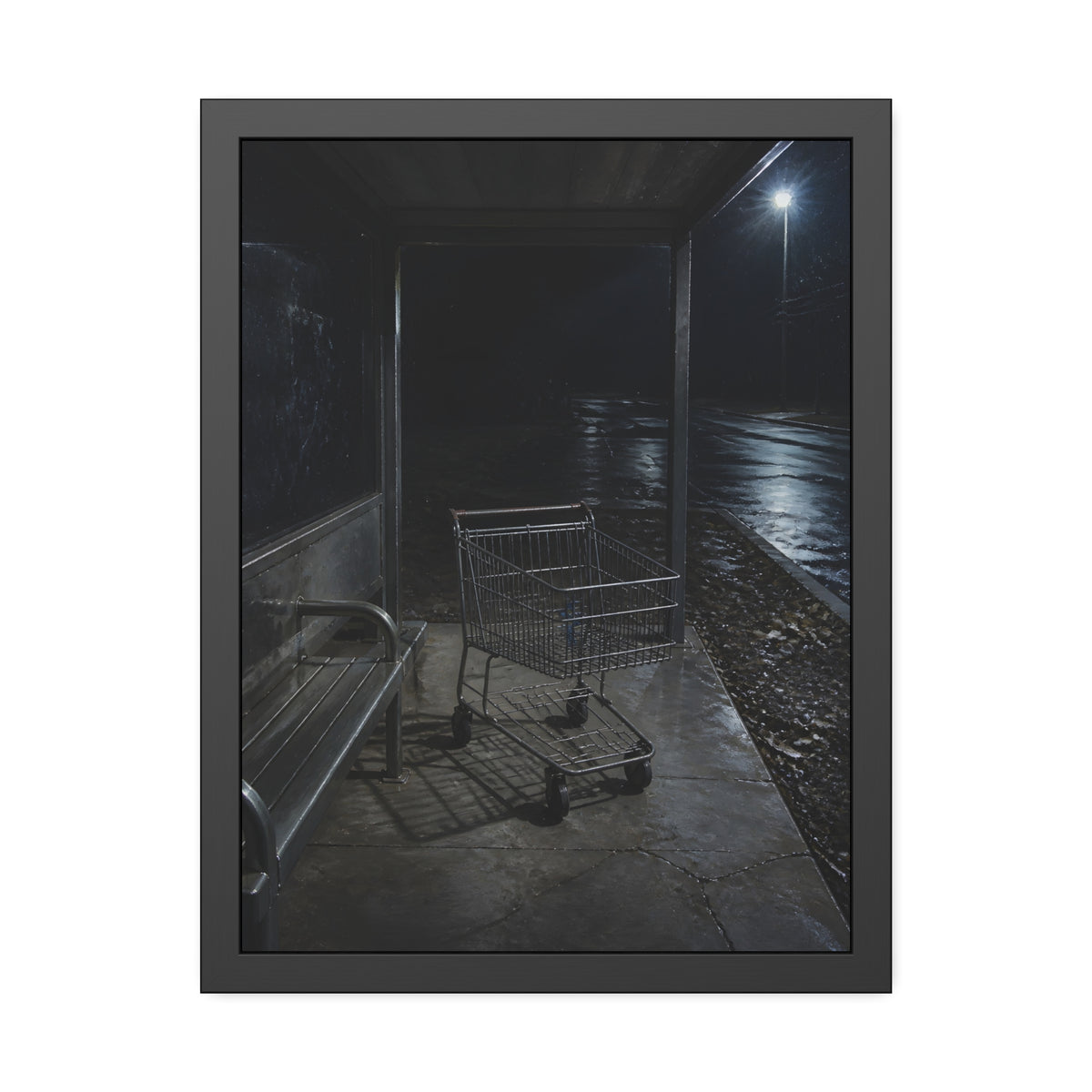 A shopping cart parked inside a bus shelter under a street lamp at night. The Rest at the Bus Shelter by Garabaggio, framed fine art print, 18″ x 24″.