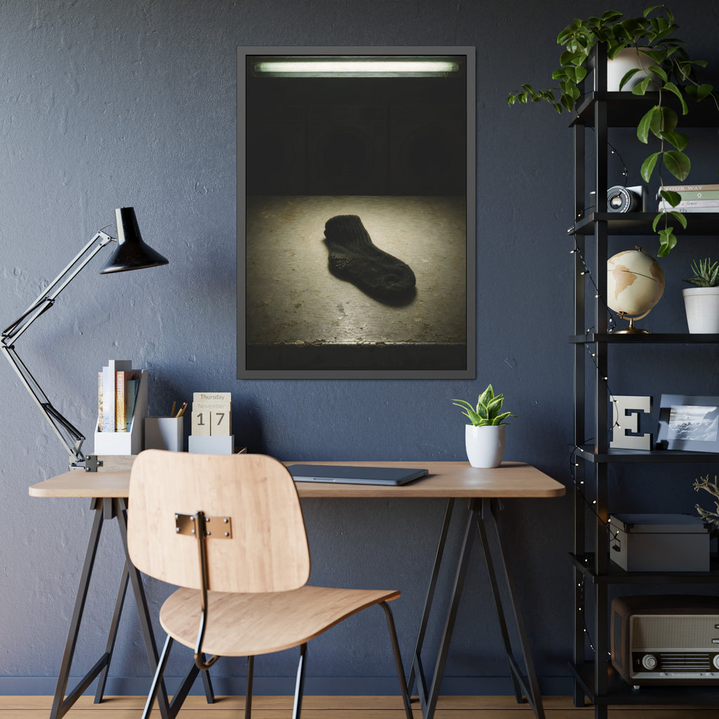 A single dark sock on a laundromat floor before dim washing machines. The Orphaned Sock by Garabaggio, framed fine art print hanging in a room.