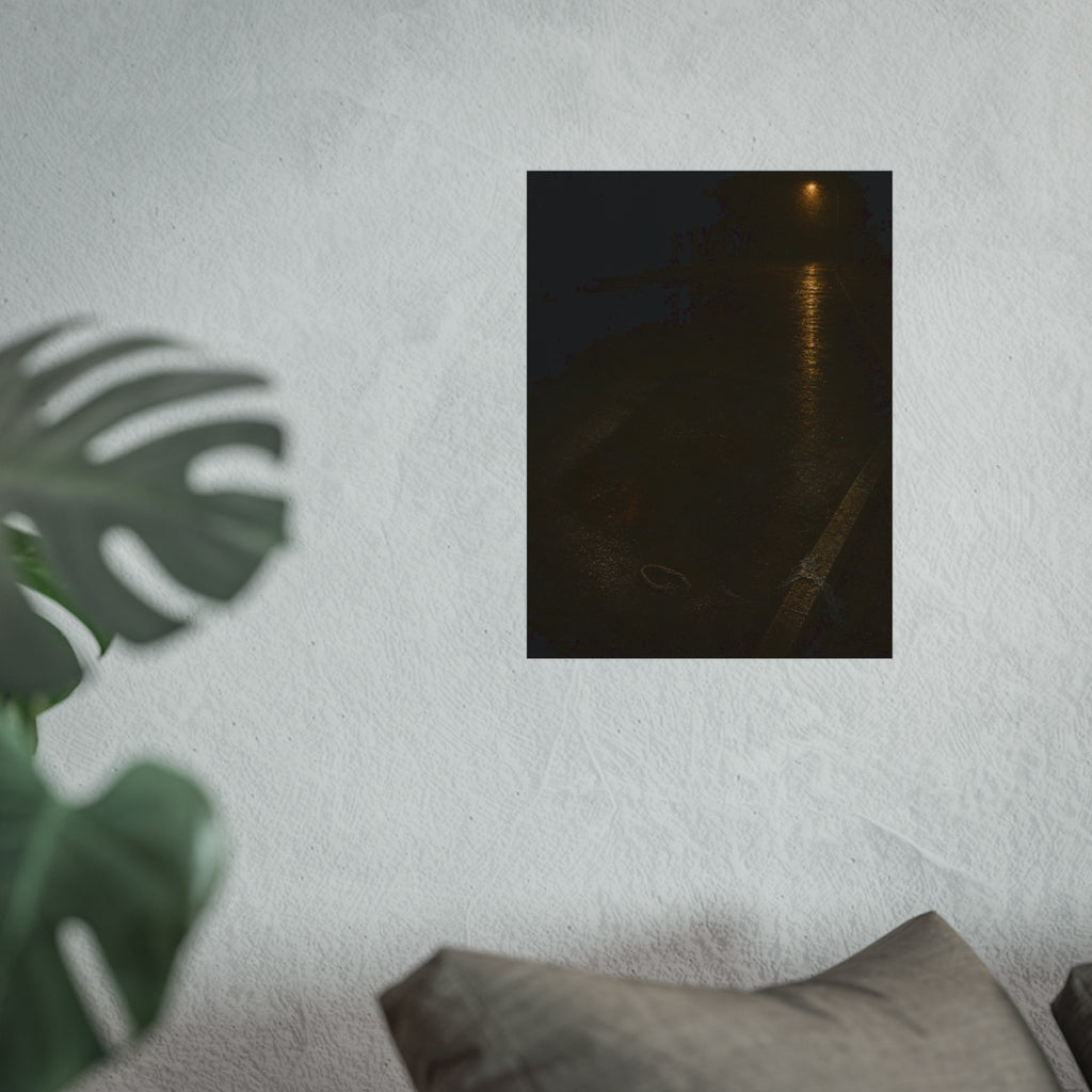 A rectangular stain on wet asphalt where something lay, under a streetlamp. The Stain After Removal by Garabaggio, fine art print hanging in a room.