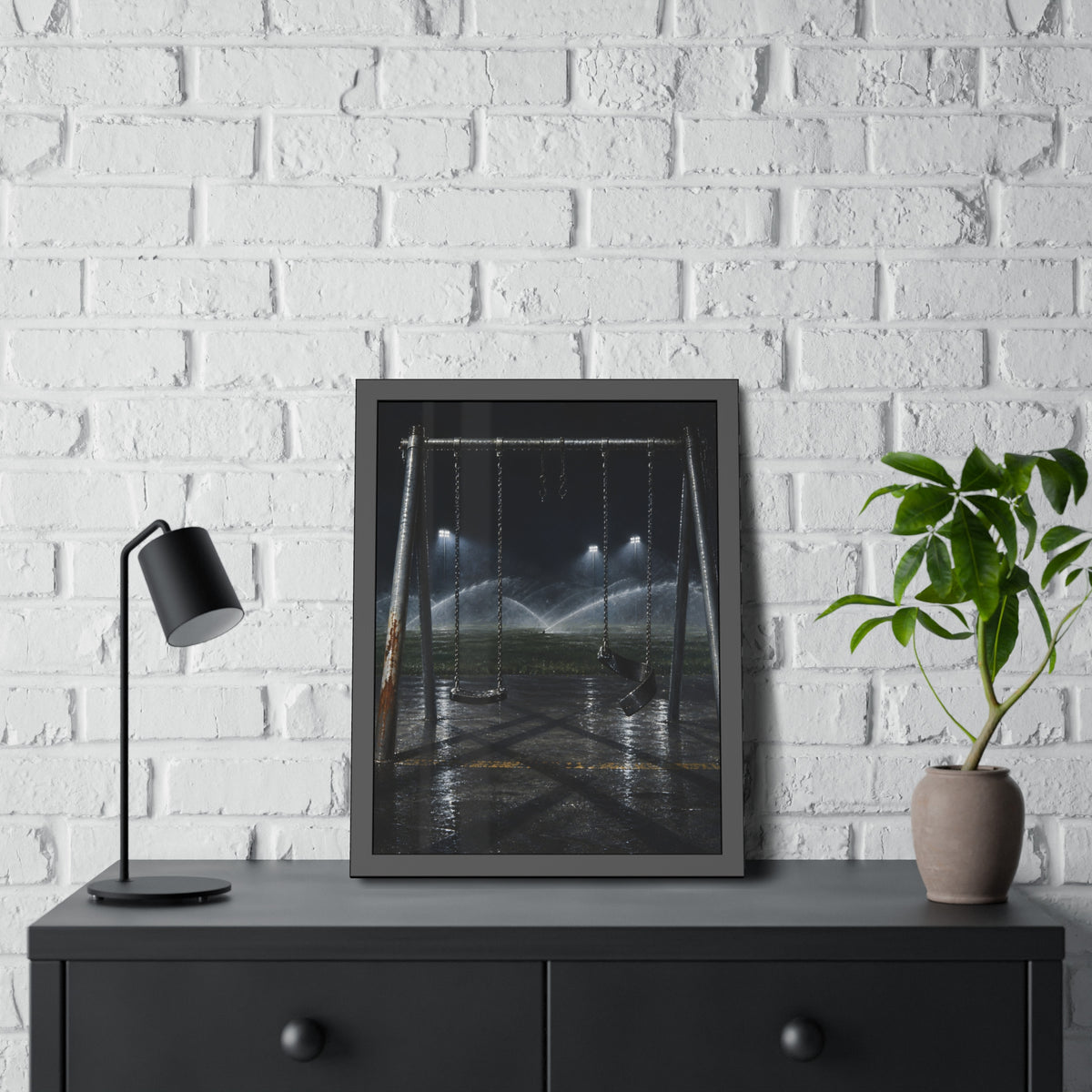 An empty swing set on wet asphalt, sprinklers arcing over the field. The Eleventh Hour: The Sprinklers by Garabaggio, framed fine art print hanging in a room.
