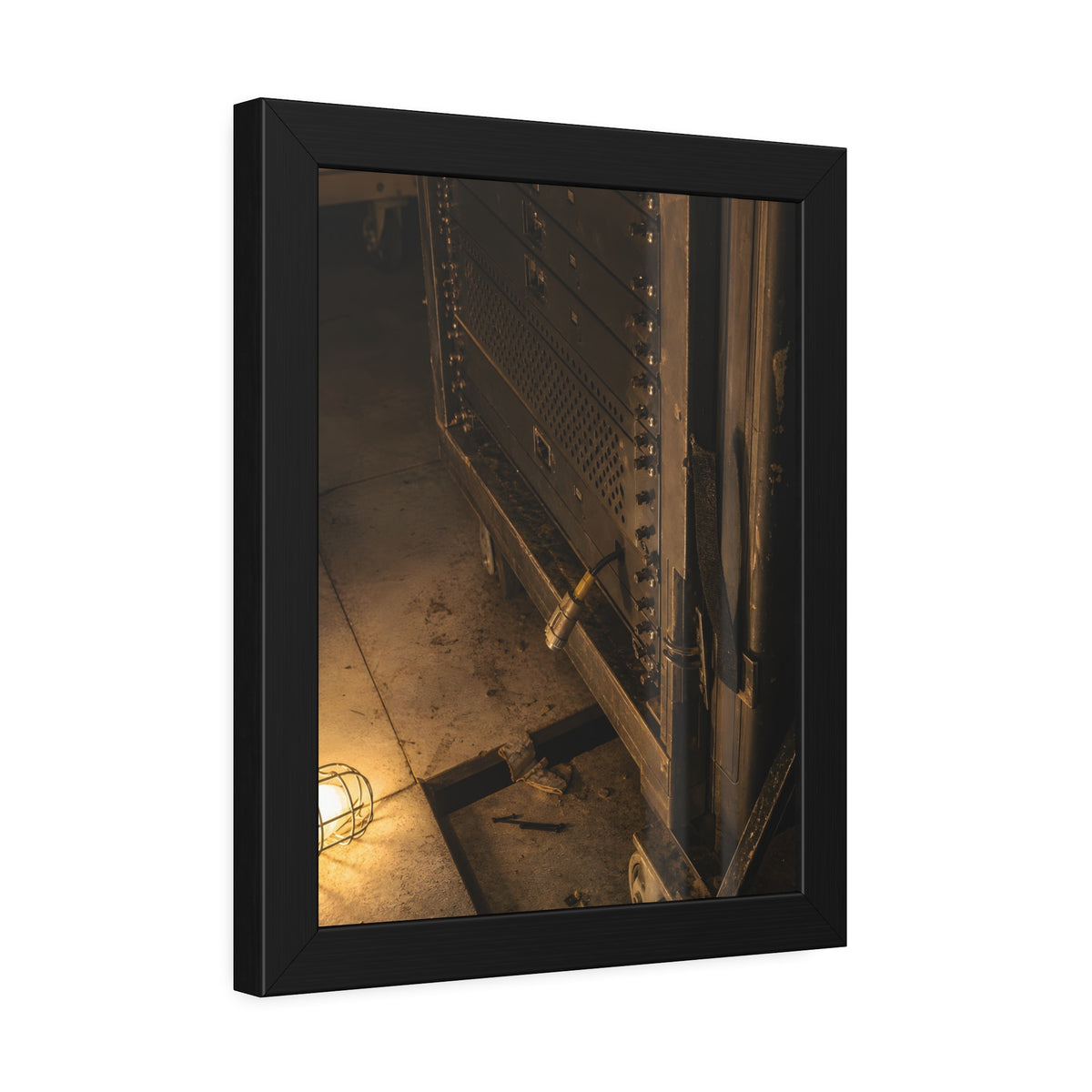 A server rack on a concrete floor beside a caged work light. The Silence at Cutover by Garabaggio, framed fine art print hanging in a room.