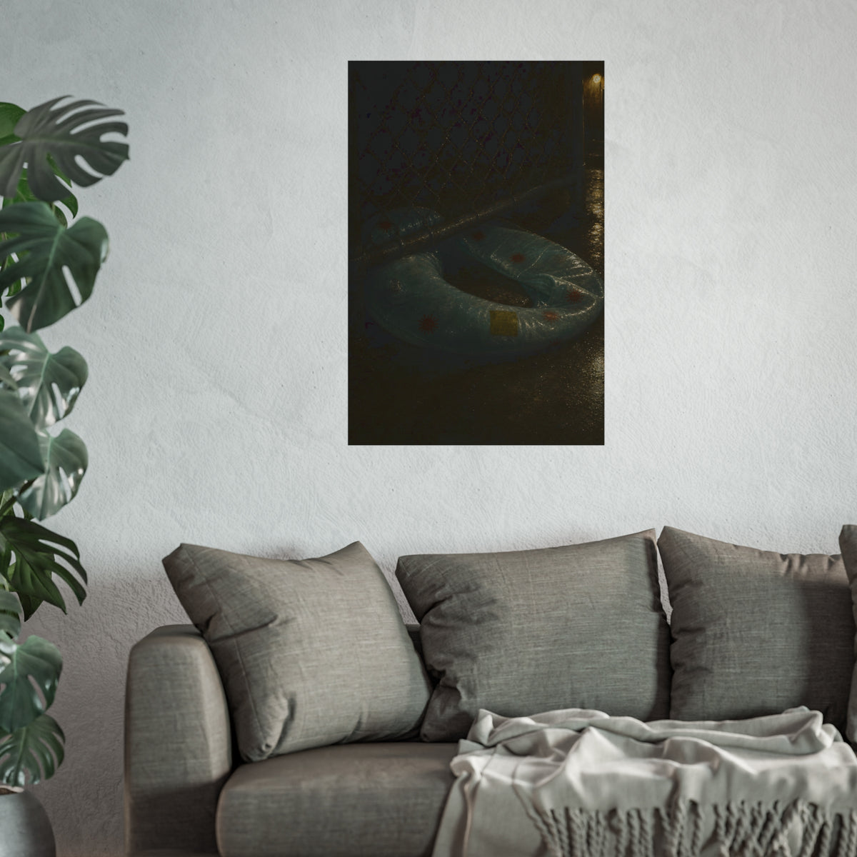 A deflated ring float pushed under a chain link fence in a wet alley. The Escape Beneath the Fence by Garabaggio, fine art print hanging in a room.
