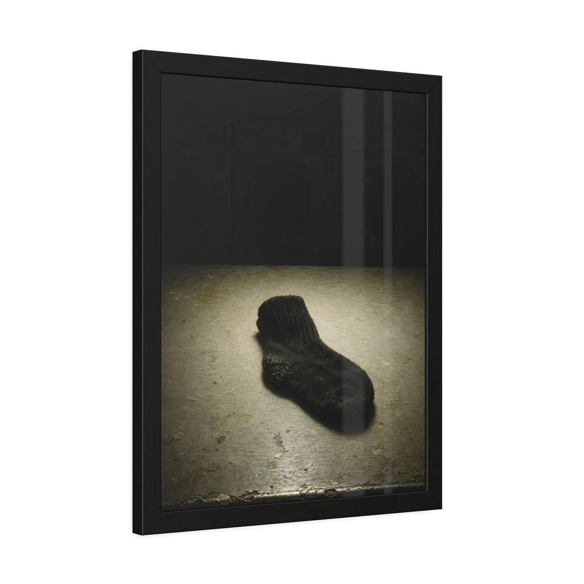 A single dark sock on a laundromat floor before dim washing machines. The Orphaned Sock by Garabaggio, framed fine art print hanging in a room.