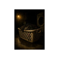 A laundry basket heaped with wet dark clothes under a bare bulb. The Burden of Wet Clothes by Garabaggio, fine art print, 12″ x 16″.