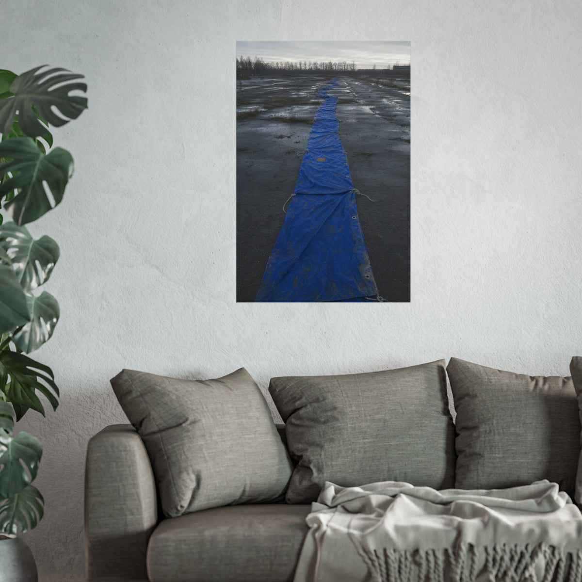 A blue tarp laid in a long strip down a wet cracked lot under grey sky. The Long Ground Procession by Garabaggio, fine art print hanging in a room.