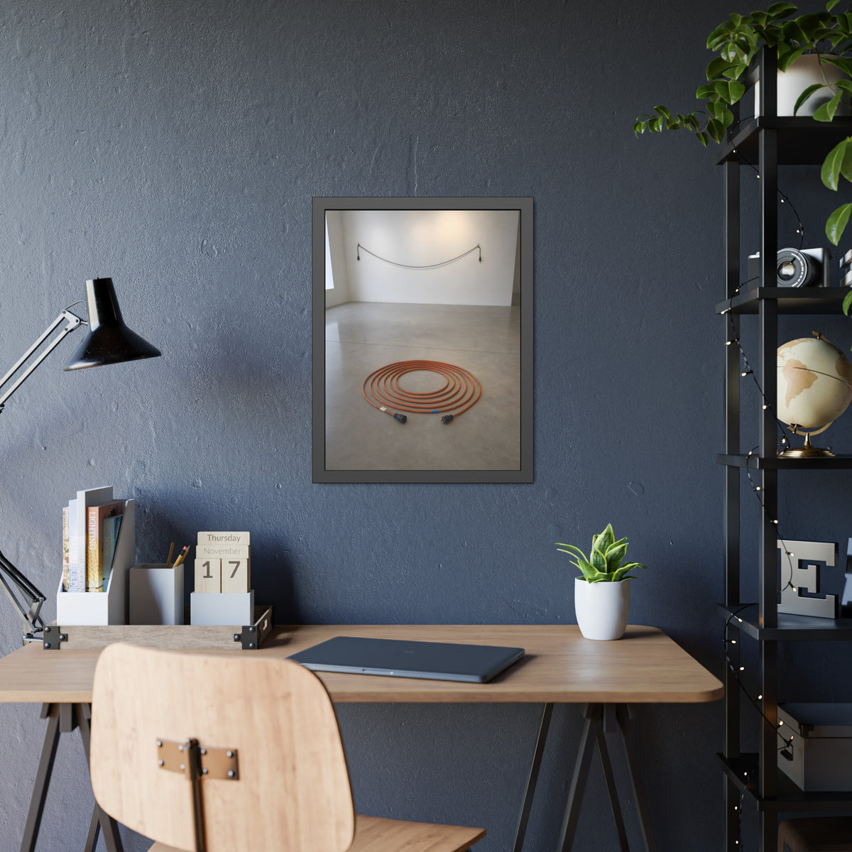 An orange extension cord coiled in a spiral on a bare gallery floor. The Floor Coil by Garabaggio, framed fine art print hanging in a room.