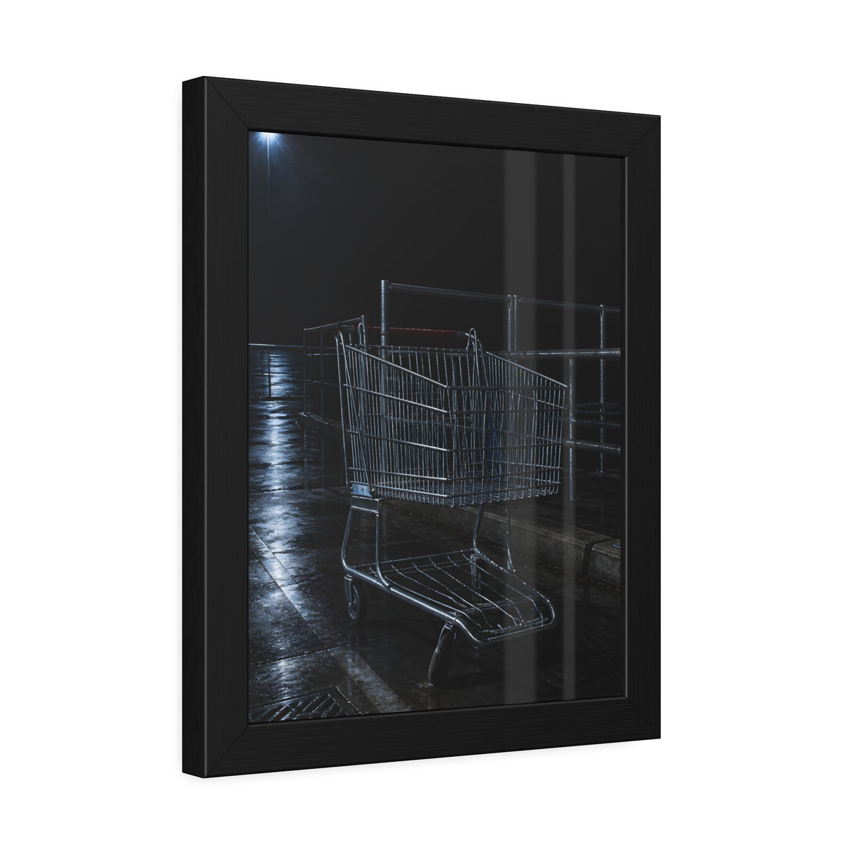 A shopping cart beside its corral on wet asphalt under a lot light. The Cart at the Corral by Garabaggio, framed fine art print hanging in a room.
