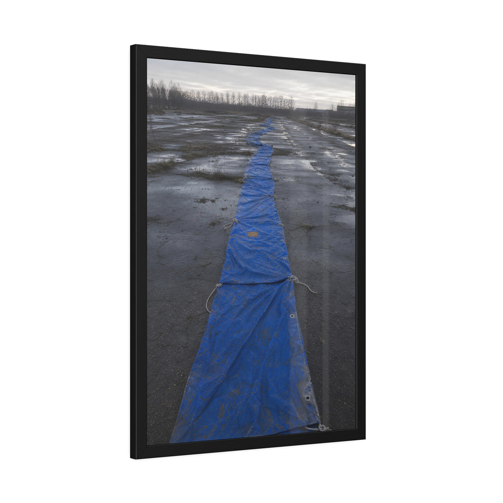 A blue tarp laid in a long strip down a wet cracked lot under grey sky. The Long Ground Procession by Garabaggio, framed fine art print hanging in a room.