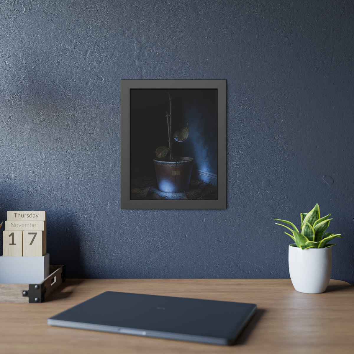 A bare potted plant dropping a leaf, dead leaves on the floor. The Leaf Lets Go by Garabaggio, framed fine art print hanging in a room.
