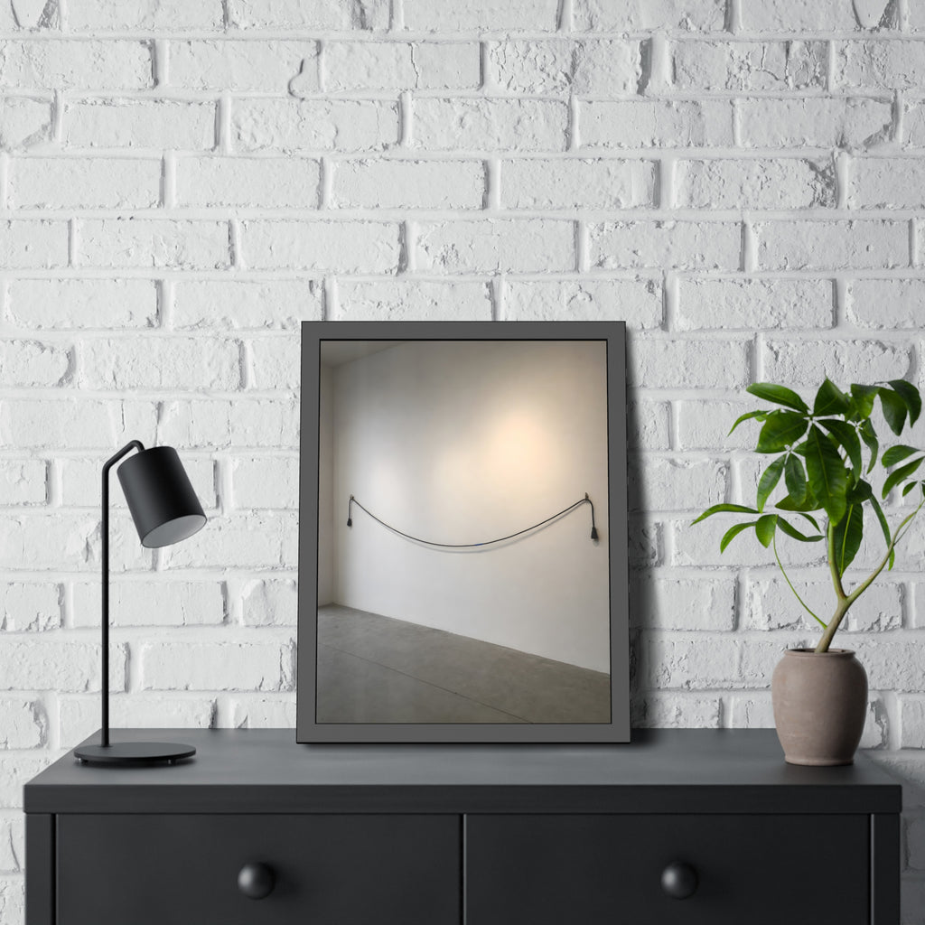 An extension cord hung in a long slack curve across a bare white wall. The Unplugged Line by Garabaggio, framed fine art print hanging in a room.