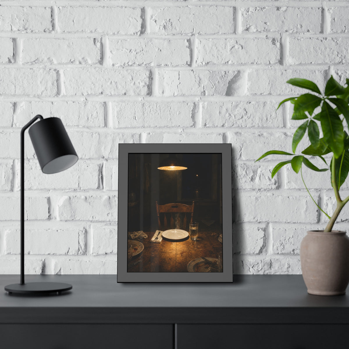 A clean plate and empty chair under a hanging lamp at a used dinner table. The Empty Seat at Dinner by Garabaggio, framed fine art print hanging in a room.