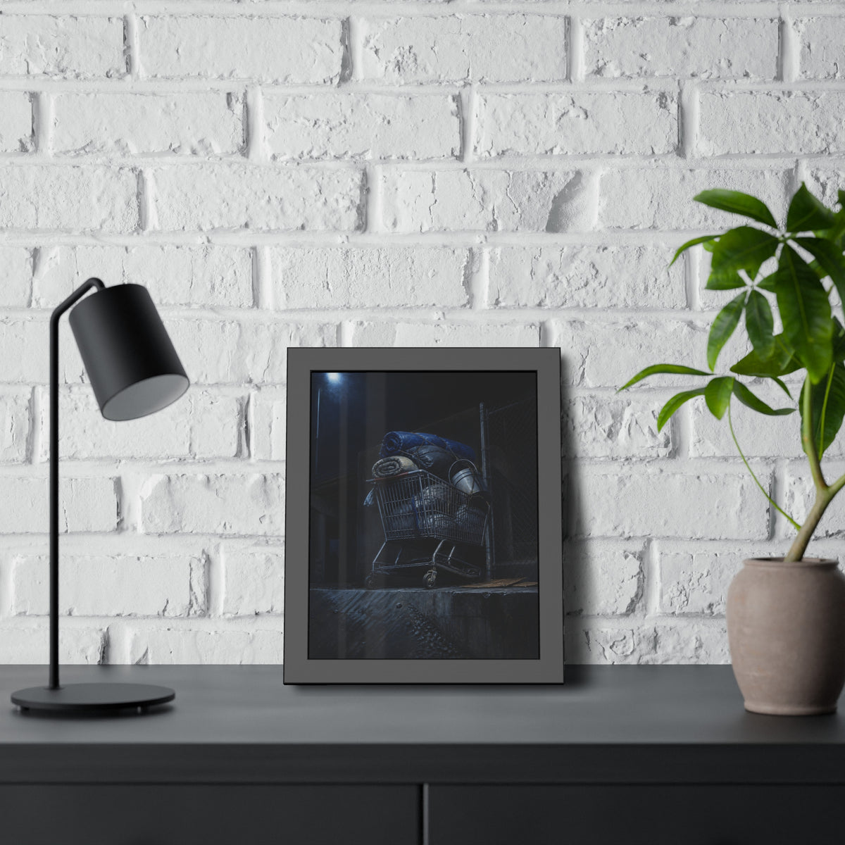 A shopping cart piled with bedding and buckets under a streetlamp. The Loading of Another Life by Garabaggio, framed fine art print hanging in a room.