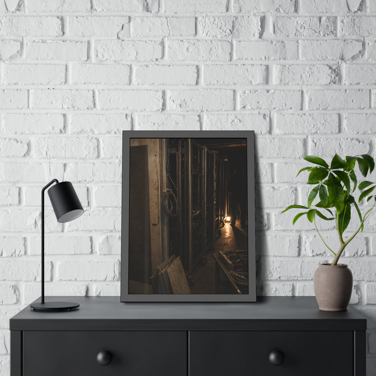 Open server racks in a dark room, a work lamp and a figure at the end. Garabaggio at the End of the Row by Garabaggio, framed fine art print hanging in a room.