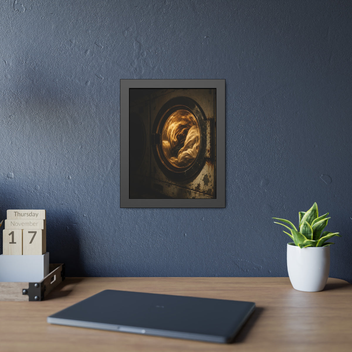 A washer drum tumbling laundry lit amber behind its glass door. The First Spin by Garabaggio, framed fine art print hanging in a room.