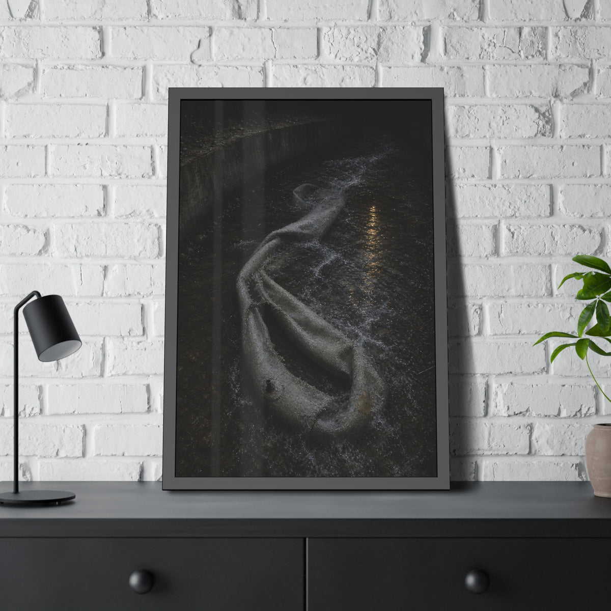 A deflated pool float caught in a concrete drainage channel of running water. The Release into Runoff by Garabaggio, framed fine art print hanging in a room.