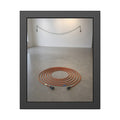 An orange extension cord coiled in a spiral on a bare gallery floor. The Floor Coil by Garabaggio, framed fine art print, 11″ x 14″.