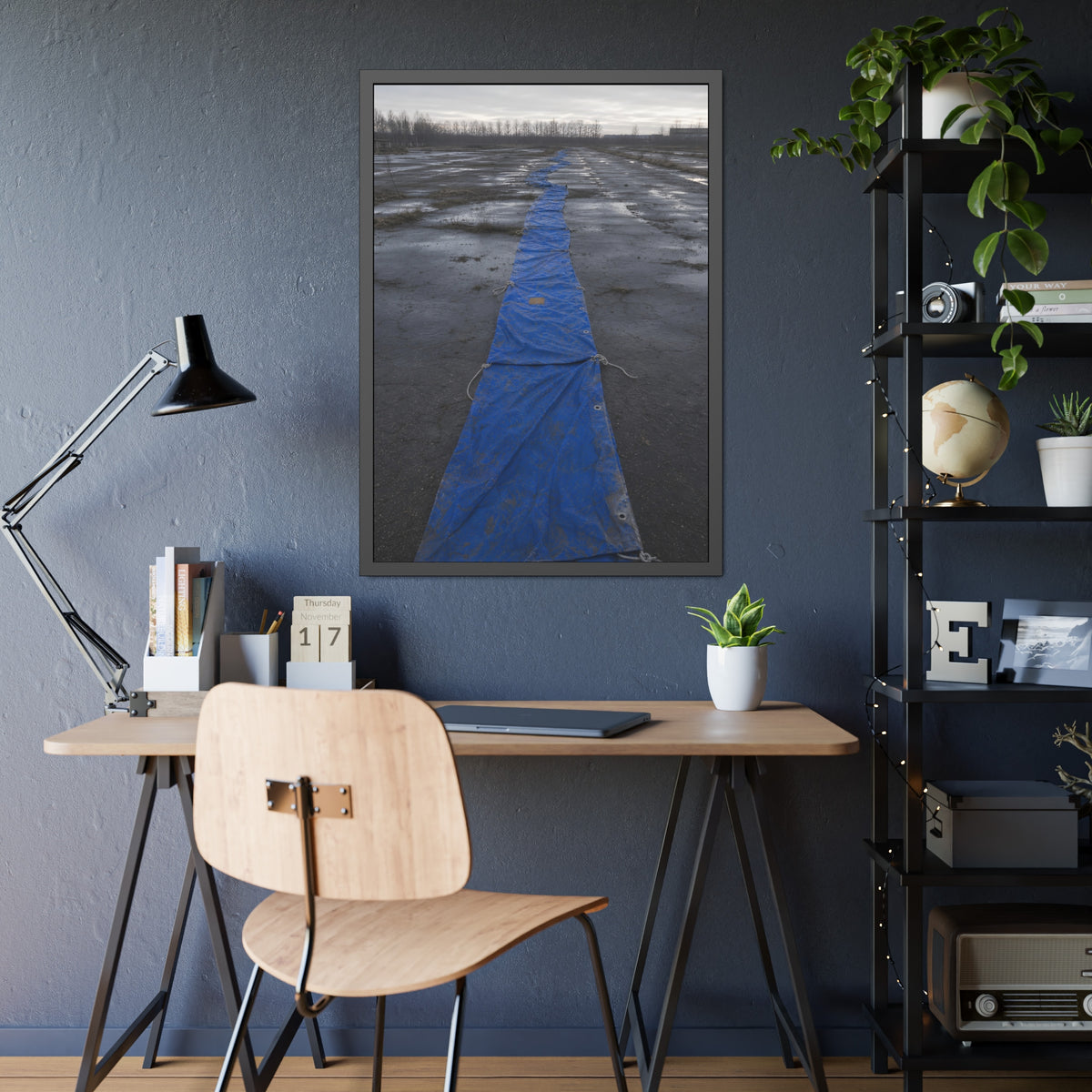 A blue tarp laid in a long strip down a wet cracked lot under grey sky. The Long Ground Procession by Garabaggio, framed fine art print hanging in a room.
