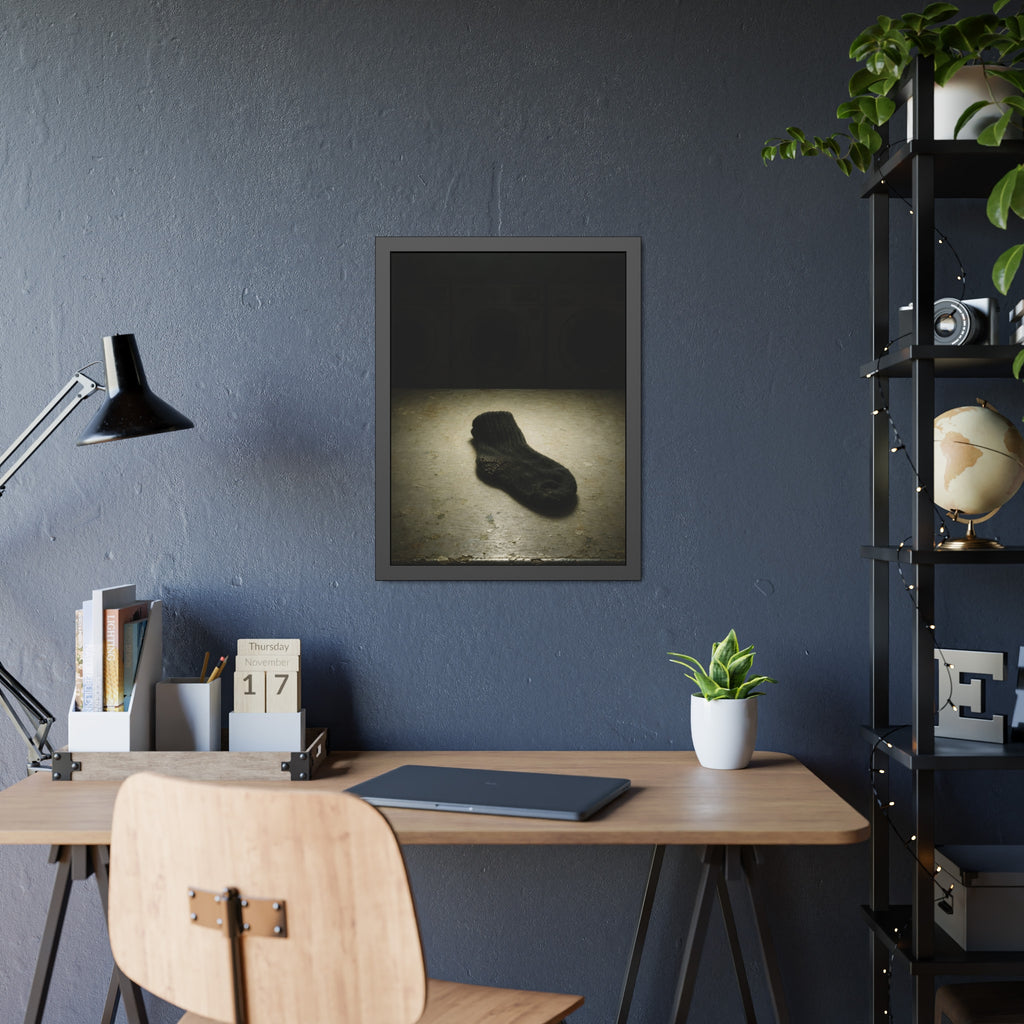 A single dark sock on a laundromat floor before dim washing machines. The Orphaned Sock by Garabaggio, framed fine art print hanging in a room.