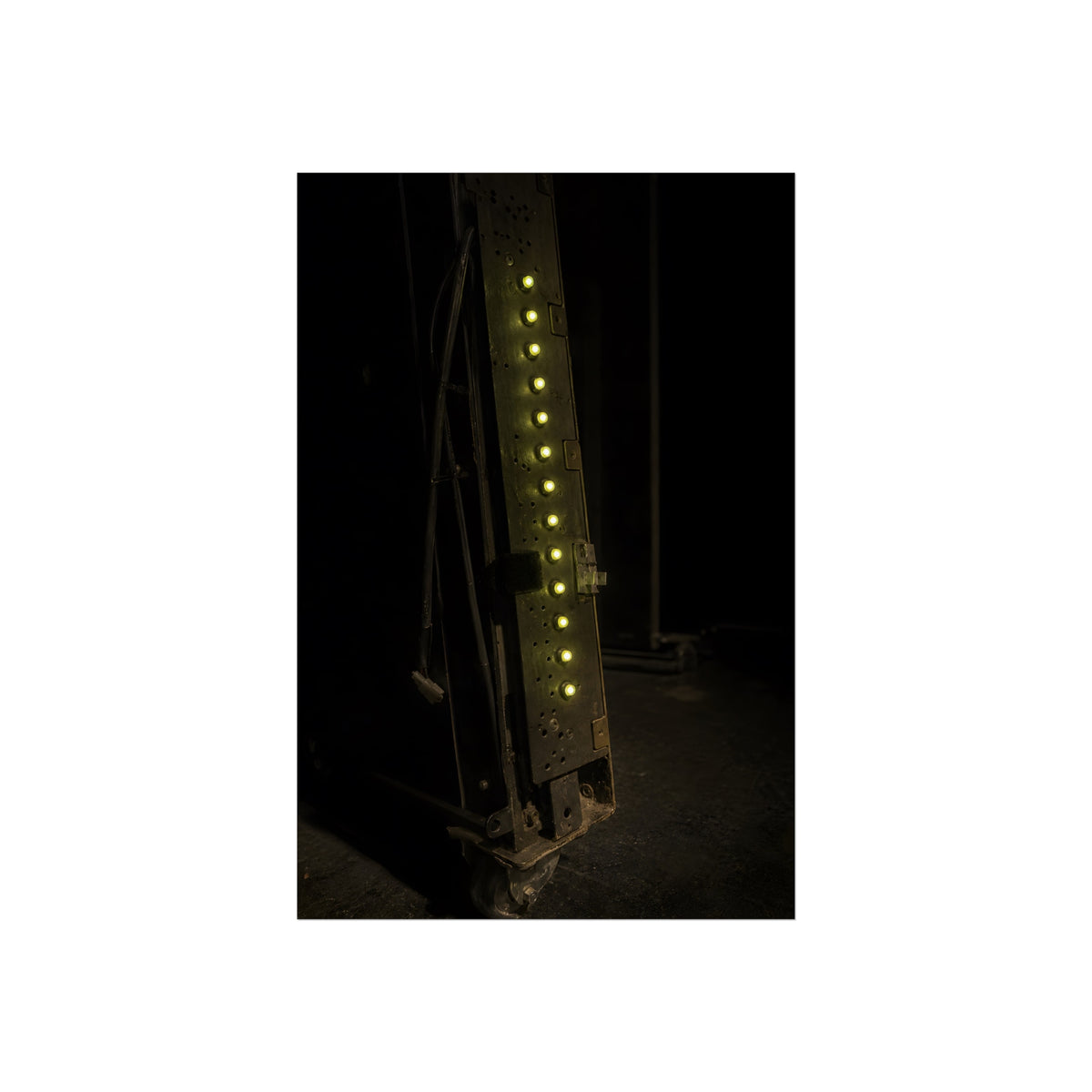 A dark rack panel with a vertical row of glowing green indicator lights. The First Green Choir by Garabaggio, fine art print, 24″ x 36″.