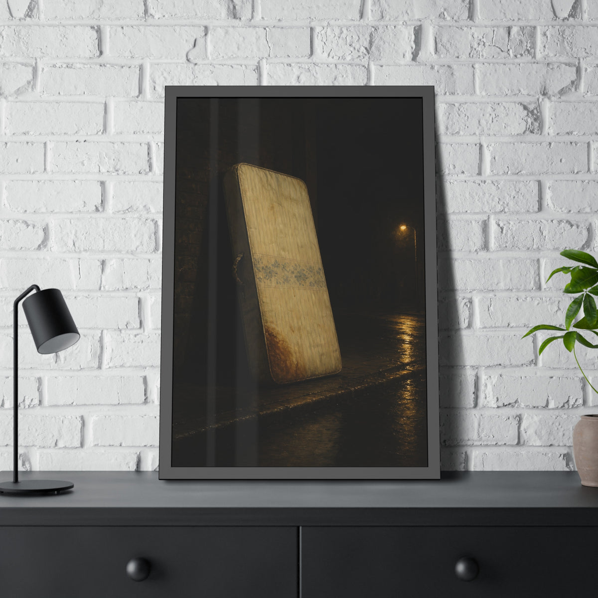A stained mattress propped on a brick wall along a wet night street. The Presentation Against the Brick by Garabaggio, framed fine art print hanging in a room.