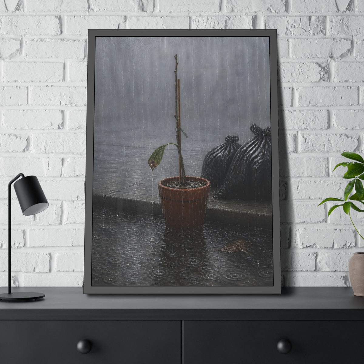 A bare stick in a clay pot on a curb in heavy rain beside trash bags. The Second Rain by Garabaggio, framed fine art print hanging in a room.