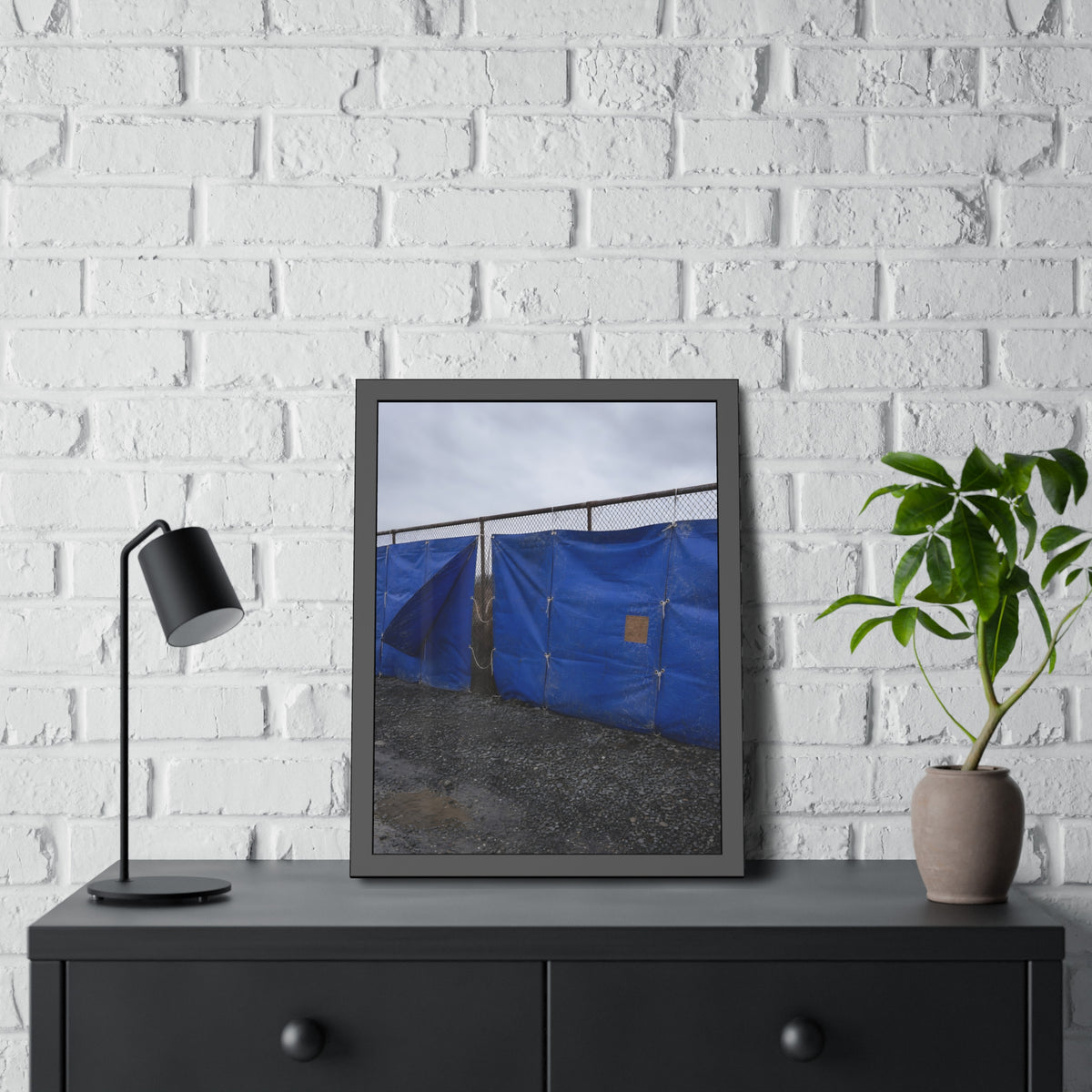 Blue tarps lashed to a chain link fence above gravel under grey sky. Drapery on the Fence by Garabaggio, framed fine art print hanging in a room.