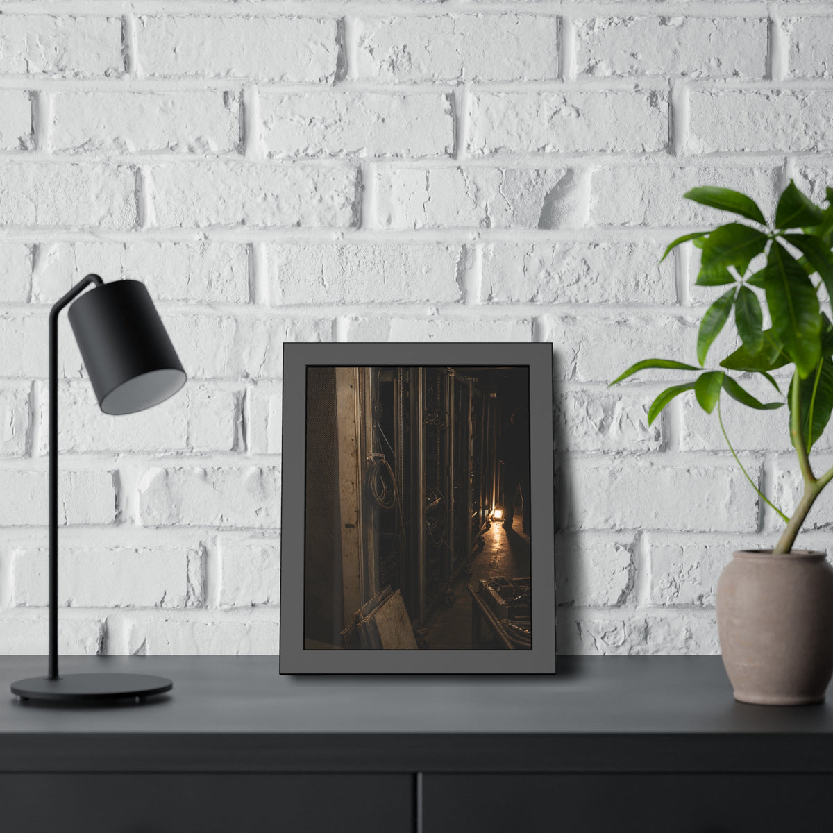 Open server racks in a dark room, a work lamp and a figure at the end. Garabaggio at the End of the Row by Garabaggio, framed fine art print hanging in a room.