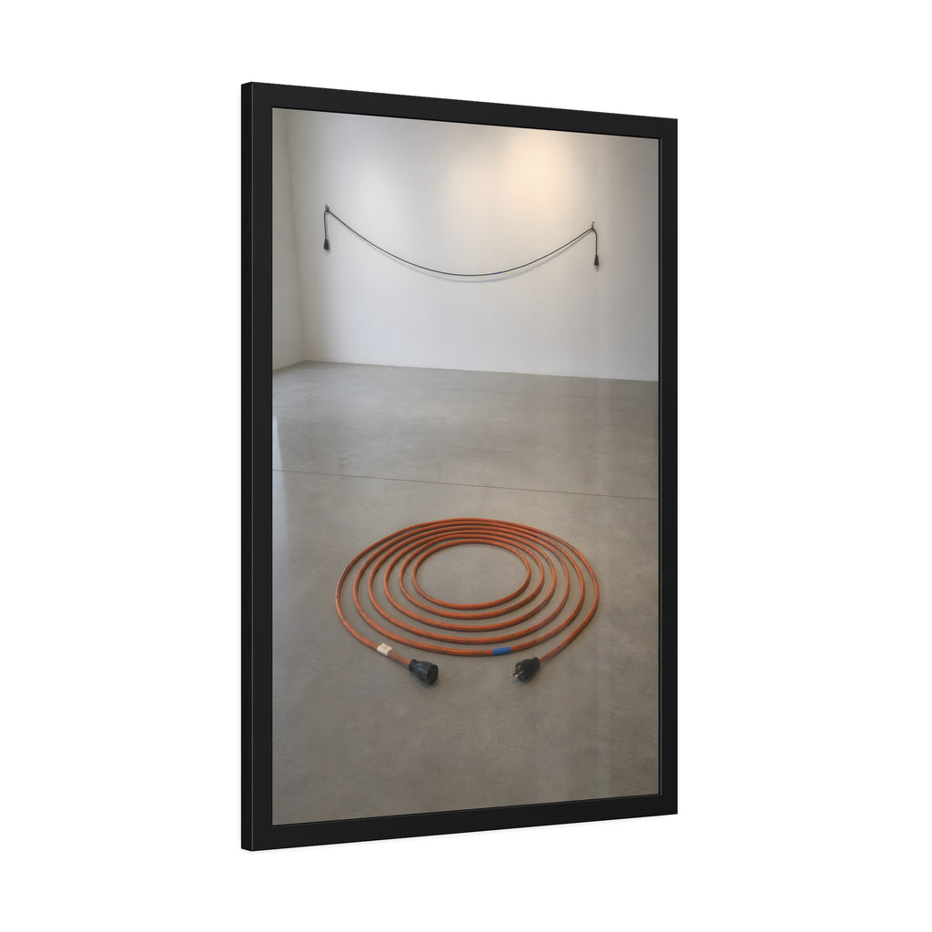 An orange extension cord coiled in a spiral on a bare gallery floor. The Floor Coil by Garabaggio, framed fine art print hanging in a room.
