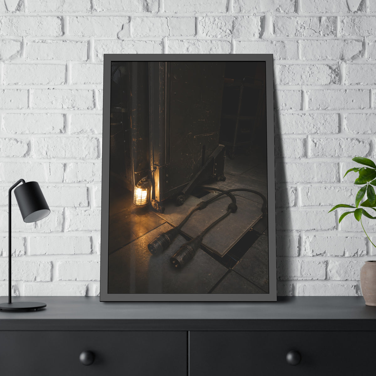 Two thick power cables unplugged on the floor beside a caged work lamp. The Redundant Power by Garabaggio, framed fine art print hanging in a room.