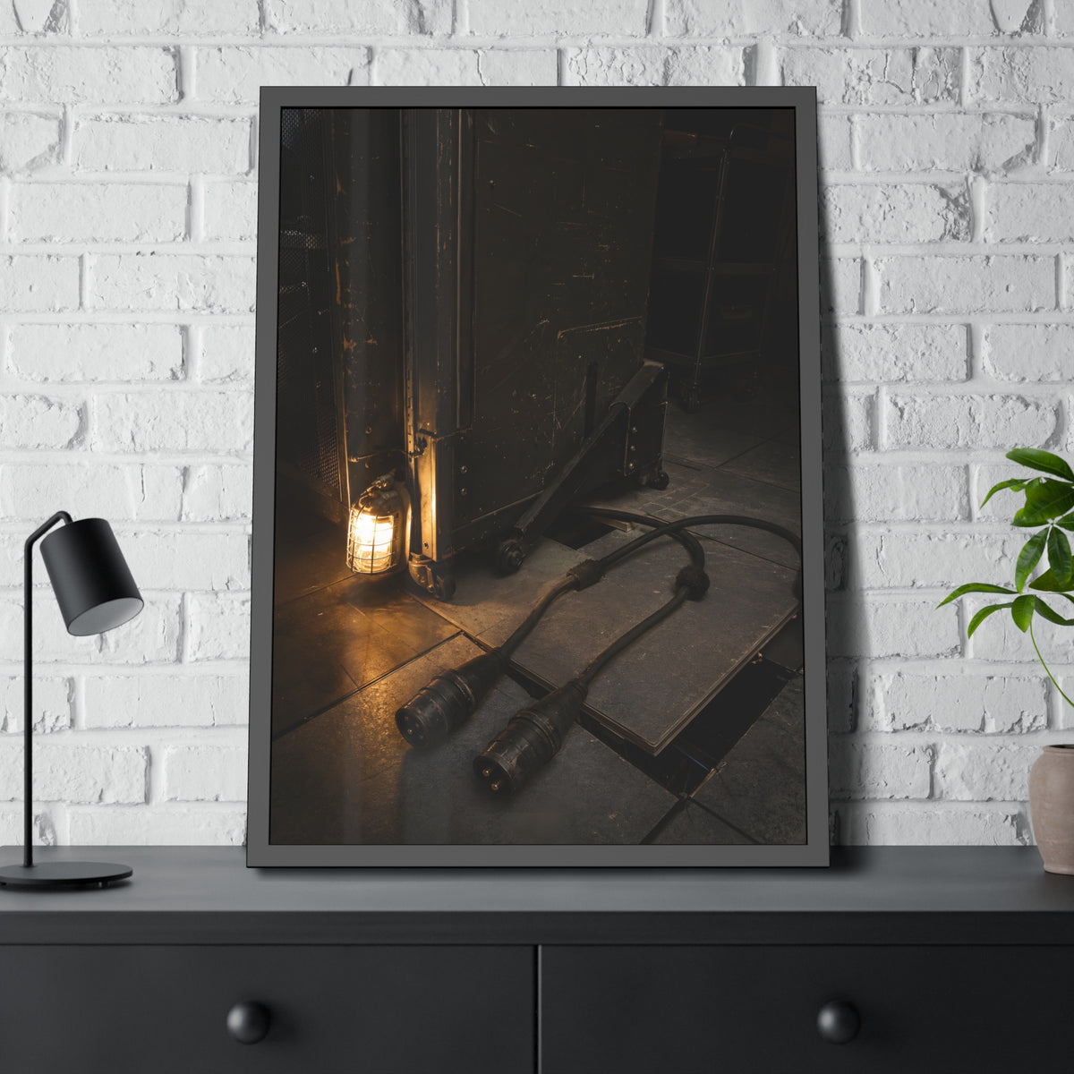 Two thick power cables unplugged on the floor beside a caged work lamp. The Redundant Power by Garabaggio, framed fine art print hanging in a room.