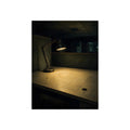 A lit desk lamp on an emptied office desk at night. The Desk Lamp Still Warm by Garabaggio, fine art print, 12″ x 16″.