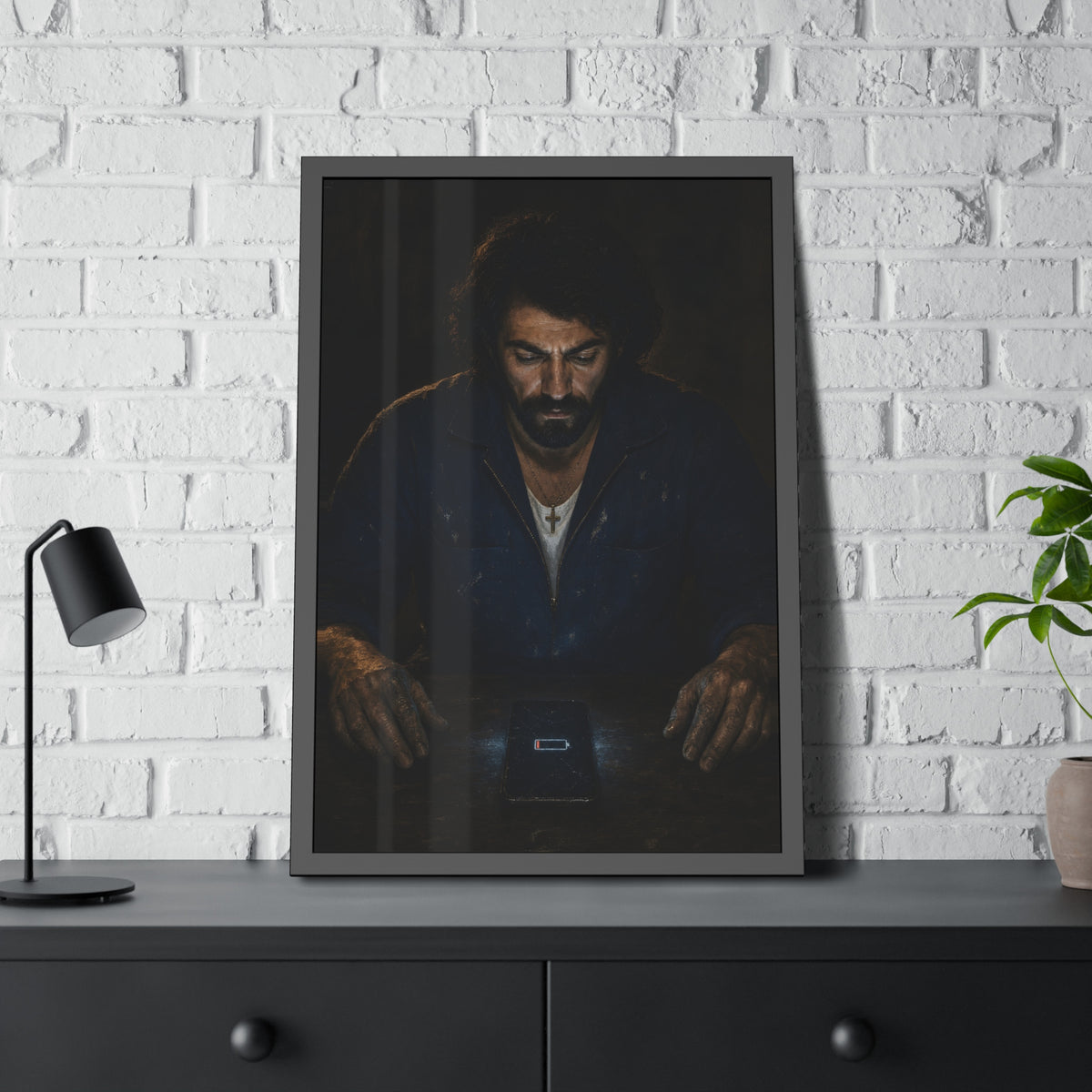A man in a work jacket looks down at a phone showing a red low battery icon. The Calling at One Percent by Garabaggio, framed fine art print hanging in a room.