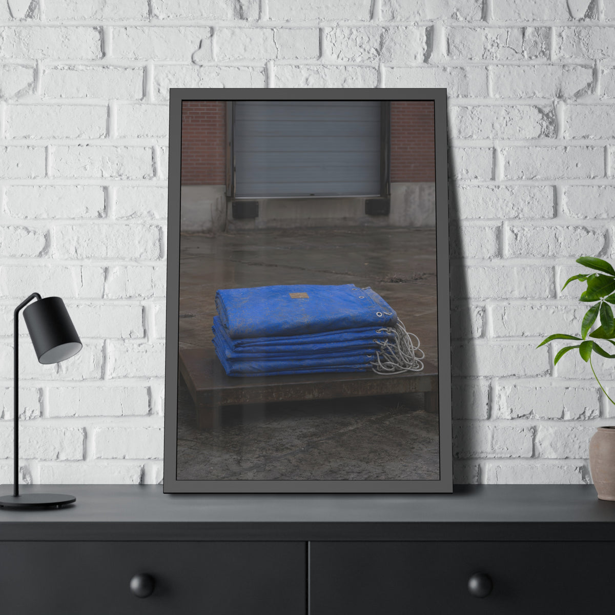 A folded blue tarp stacked on a low wooden platform by a loading dock. The Repaired Fold by Garabaggio, framed fine art print hanging in a room.