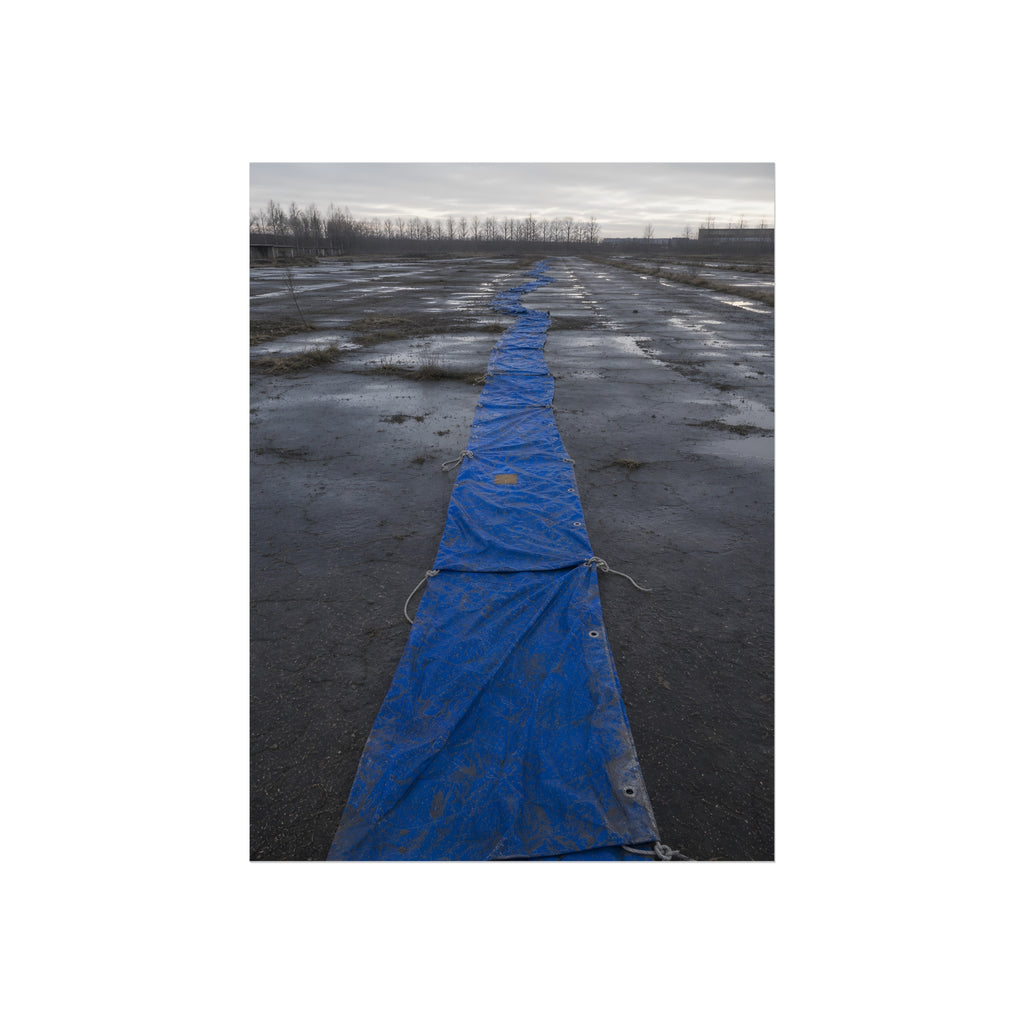 A blue tarp laid in a long strip down a wet cracked lot under grey sky. The Long Ground Procession by Garabaggio, fine art print, 12″ x 16″.