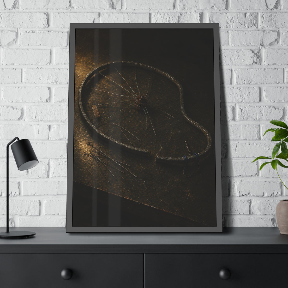 A bent bicycle wheel rim with loose spokes on a dark table in warm light. The Cutting of the Circle by Garabaggio, framed fine art print hanging in a room.