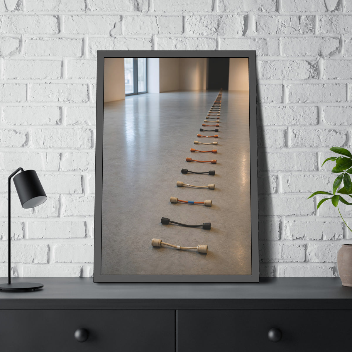 A long line of cut extension cord ends laid across a pale gallery floor. The Severed Procession by Garabaggio, framed fine art print hanging in a room.