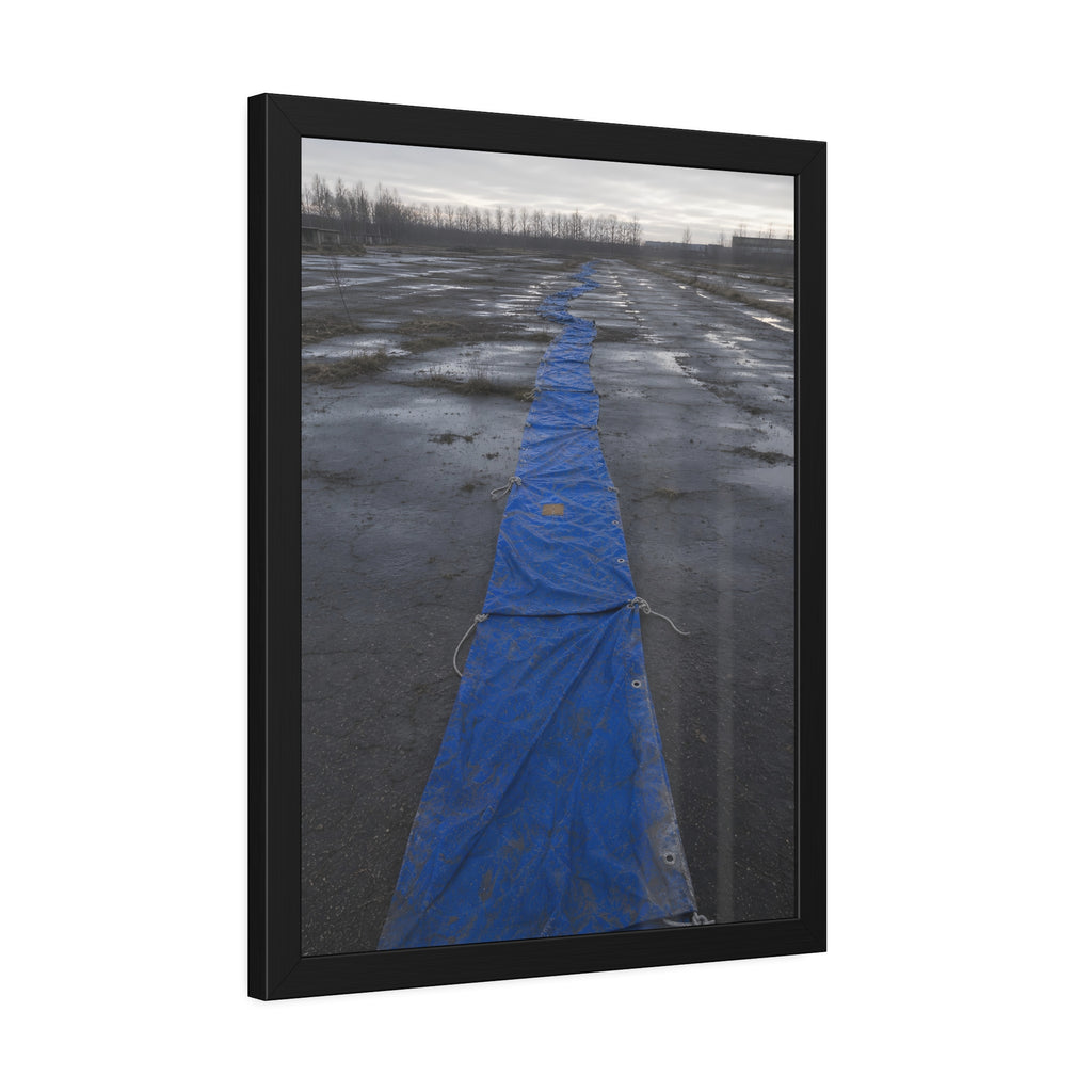 A blue tarp laid in a long strip down a wet cracked lot under grey sky. The Long Ground Procession by Garabaggio, framed fine art print hanging in a room.