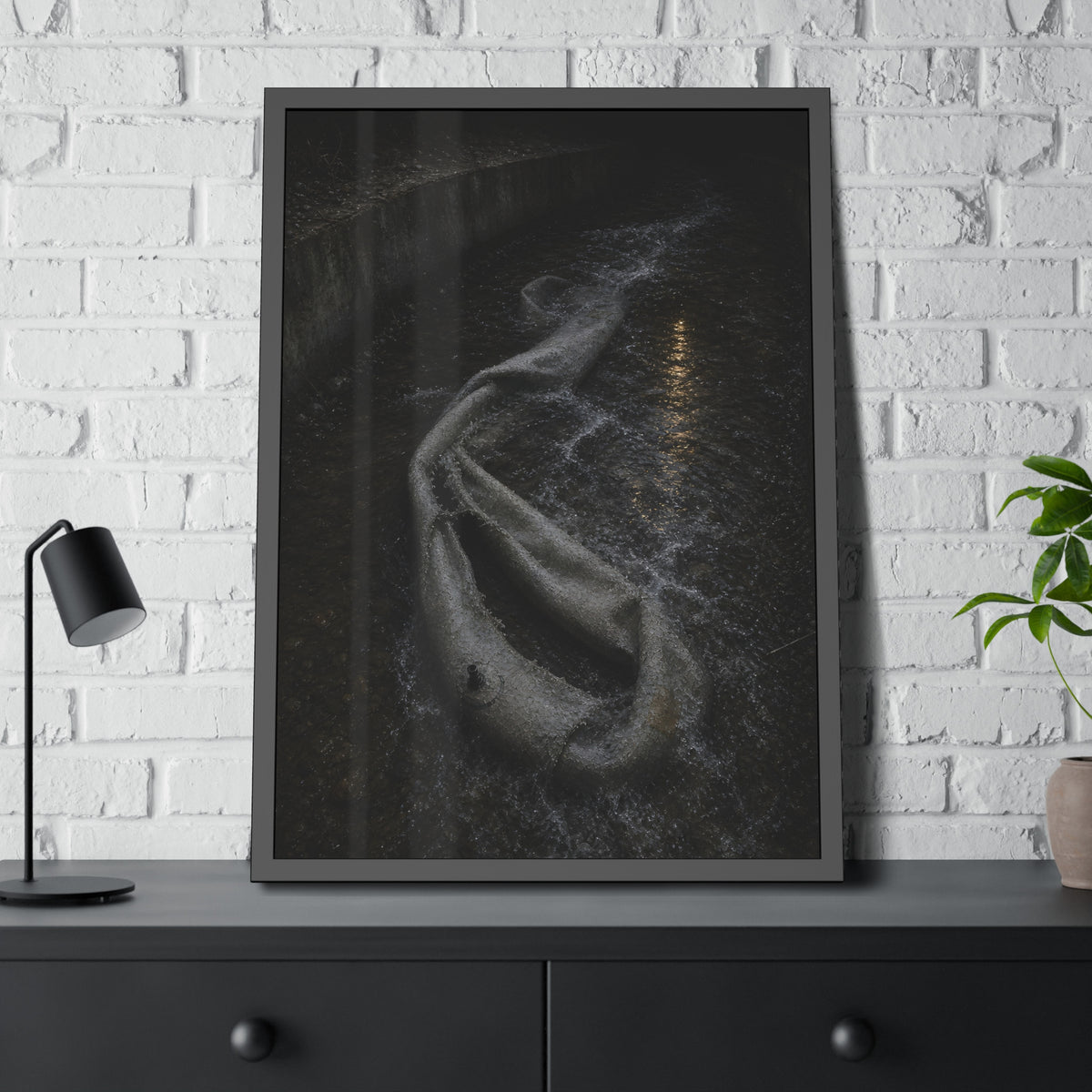 A deflated pool float caught in a concrete drainage channel of running water. The Release into Runoff by Garabaggio, framed fine art print hanging in a room.
