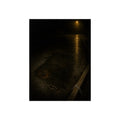 A rectangular stain on wet asphalt where something lay, under a streetlamp. The Stain After Removal by Garabaggio, fine art print, 12″ x 16″.