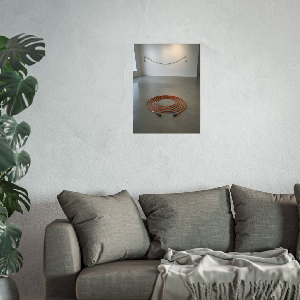 An orange extension cord coiled in a spiral on a bare gallery floor. The Floor Coil by Garabaggio, fine art print hanging in a room.