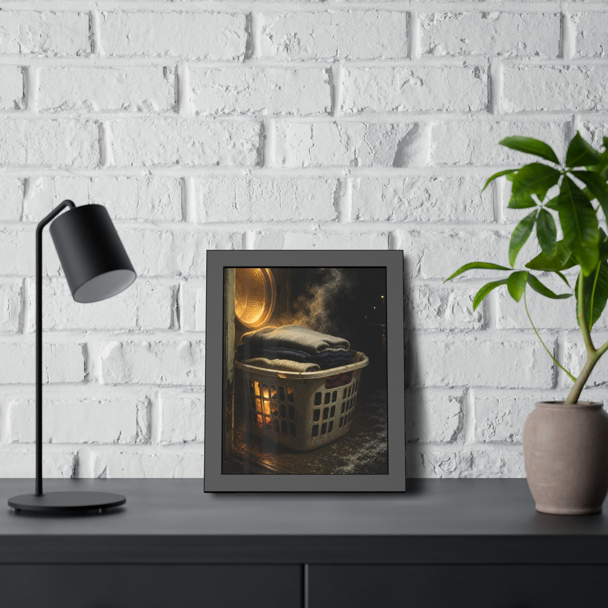 A laundry basket of folded clothes glowing in front of an open dryer. The Warm Clothes Against the Cold by Garabaggio, framed fine art print hanging in a room.