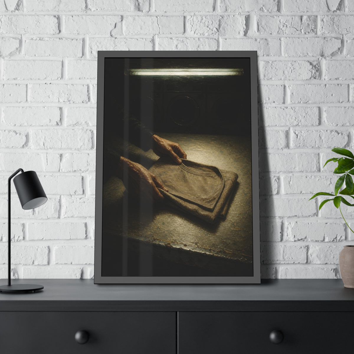 Two hands folding a shirt on a laundromat table with washers behind. The Folding at Two A.M by Garabaggio, framed fine art print hanging in a room.